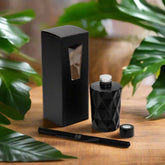 Black Oud Reed Diffuser Set on a walnut table with lush green leaves next to it